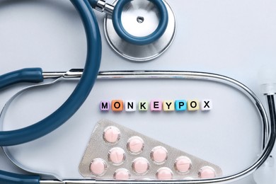 Word Monkeypox made of colorful plastic beads, pills and stethoscope on light background, flat lay