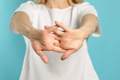 Woman cracking her knuckles on turquoise background, closeup. Bad habit