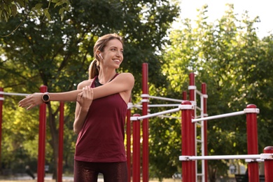 Young woman with wireless headphones listening to music while exercising on sports ground. Space for text