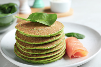 Tasty spinach pancakes with salmon on light grey table, closeup