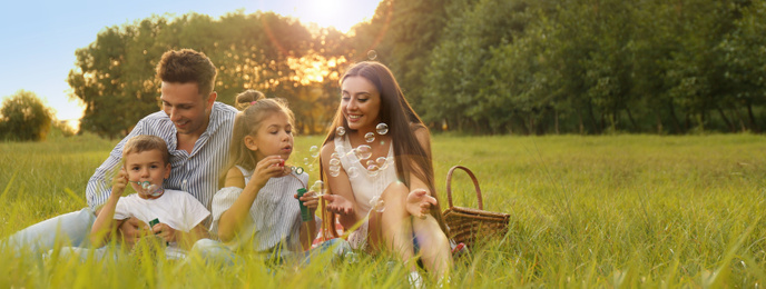 Happy family having picnic and blowing soap bubbles in park at sunset, space for text. Banner design