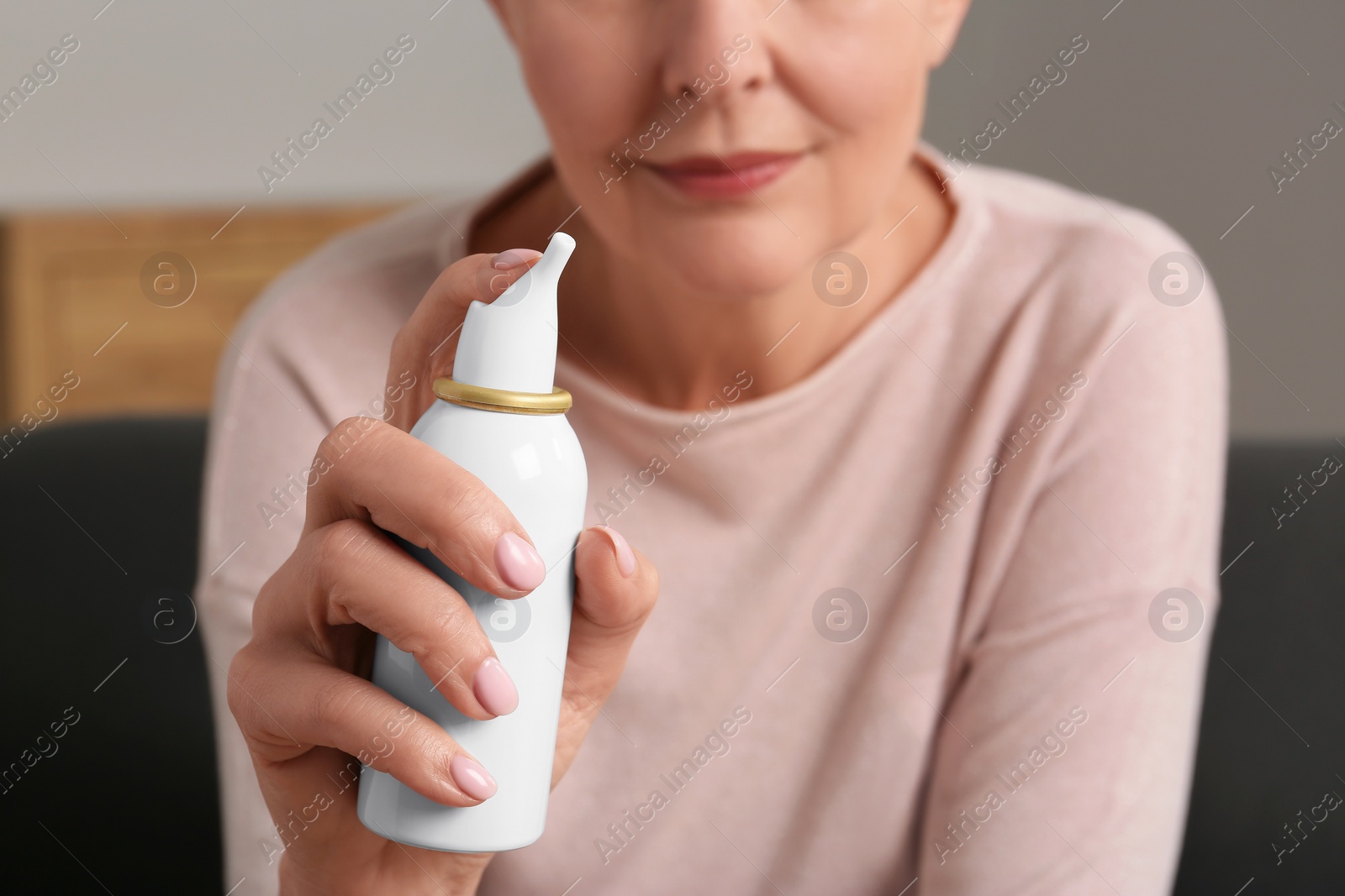 Photo of Woman holding nasal spray indoors, focus on bottle