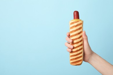 Photo of Woman holding delicious french hot dog on light blue background, closeup. Space for text