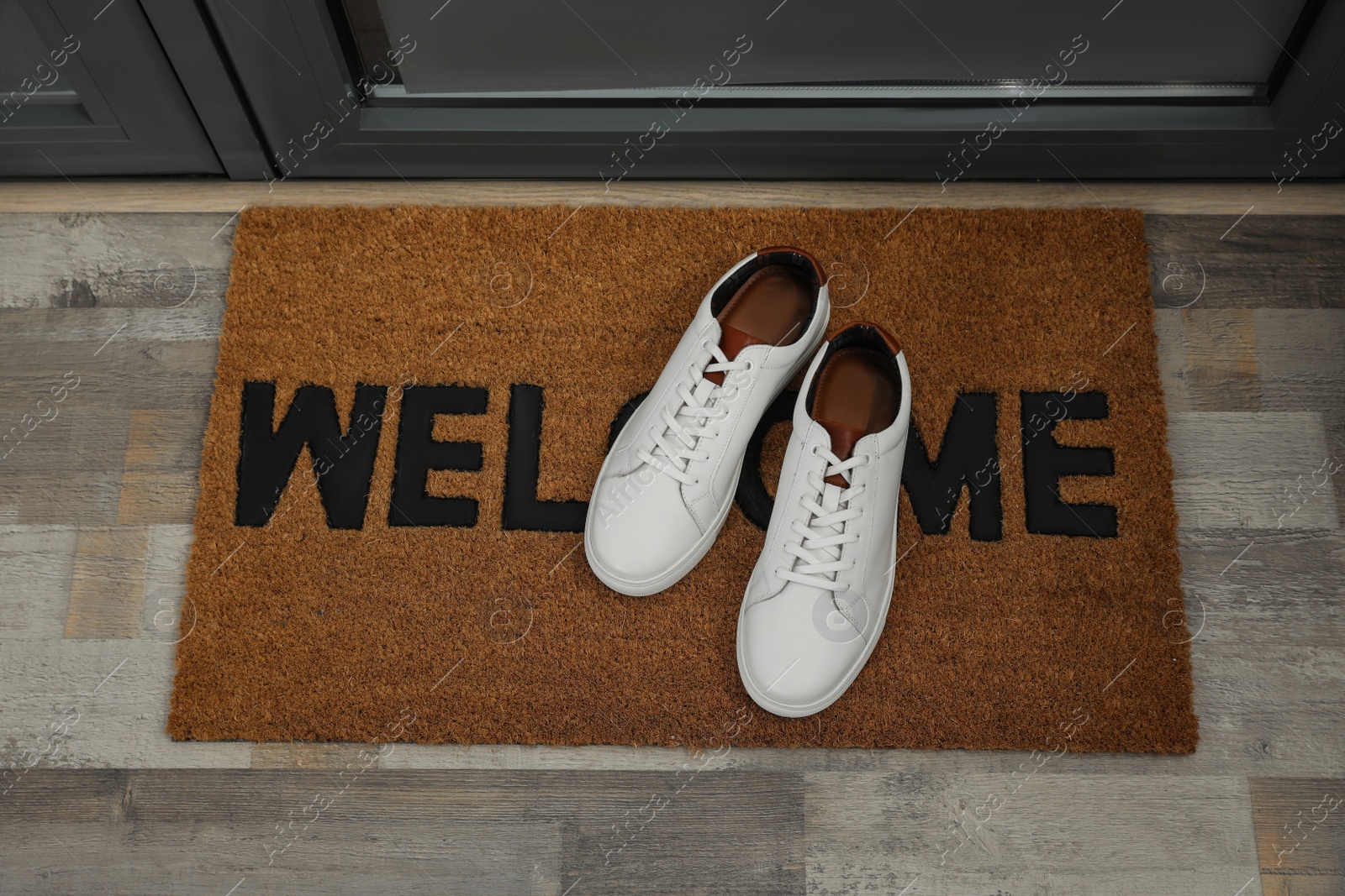 Photo of Pair of stylish white sneakers on doormat near entrance, above view