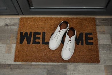Photo of Pair of stylish white sneakers on doormat near entrance, above view