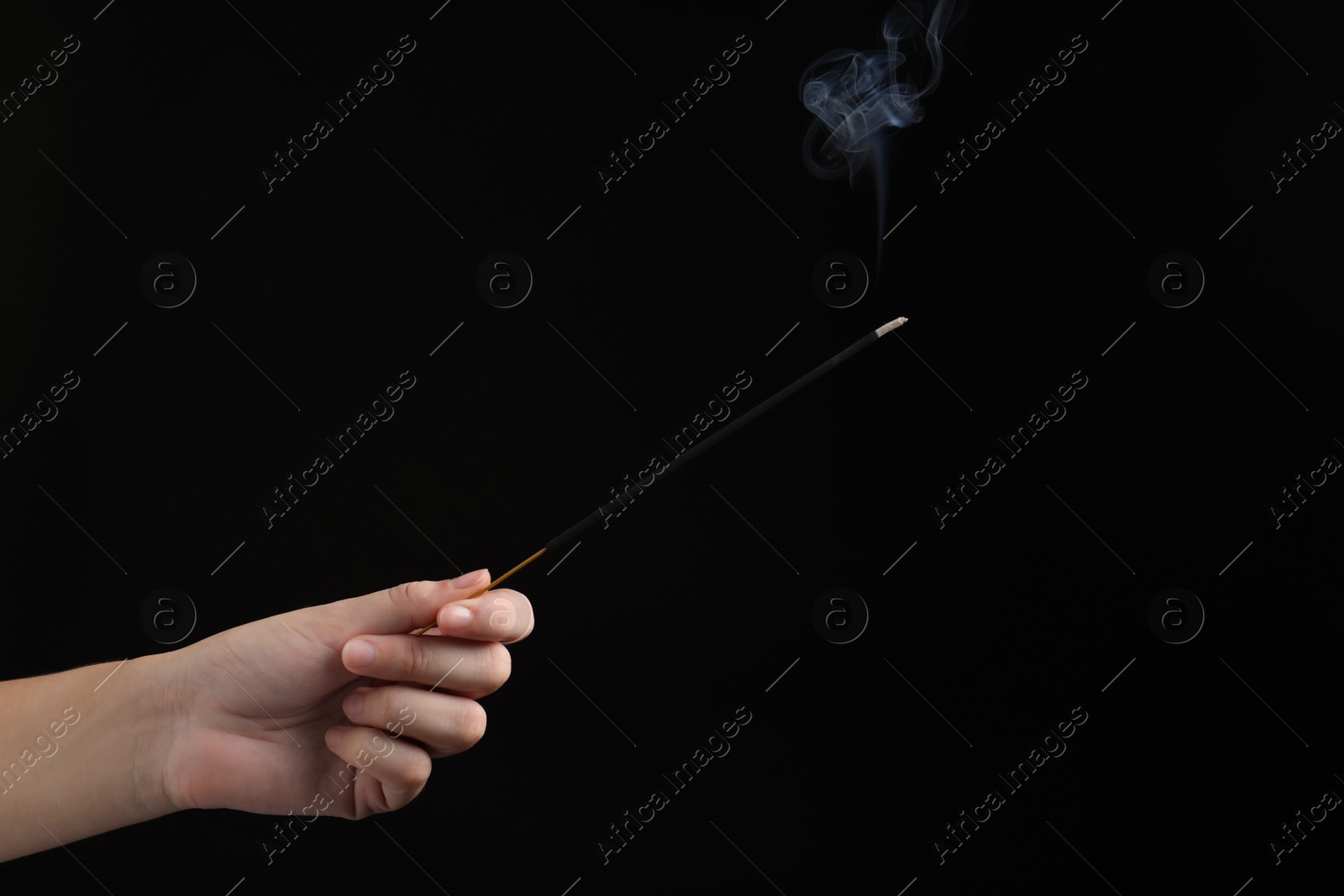 Photo of Woman holding smoldering incense stick on black background, closeup. Space for text