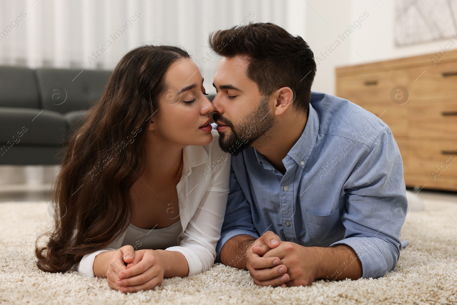 Photo of Passionate young couple kissing on soft carpet at home