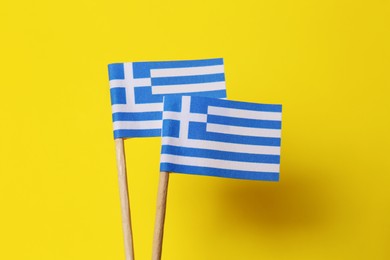 Small paper flags of Greece on yellow background, closeup