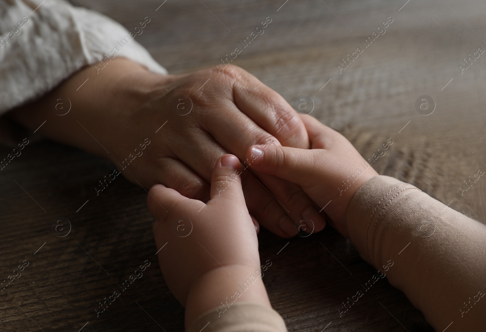 Photo of Woman holding hands with her granddaughter at wooden table, closeup