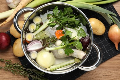 Pot and different ingredients for cooking tasty bouillon on wooden table, flat lay