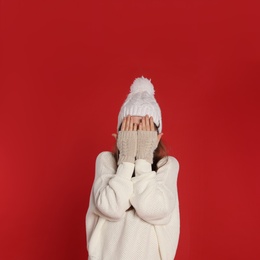 Beautiful young woman in white sweater and hat on red background. Winter season