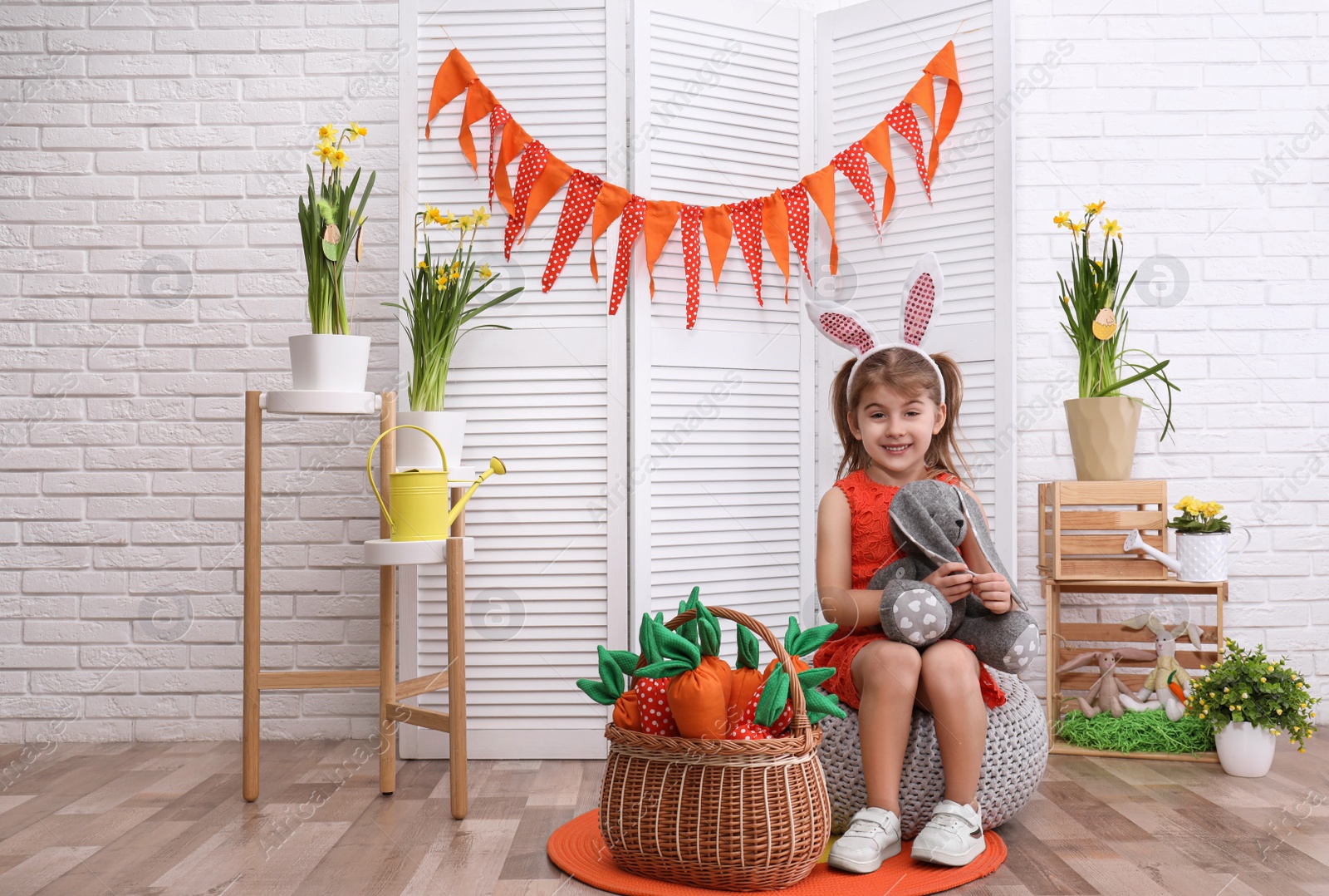 Photo of Adorable little girl with bunny ears, toy rabbit and carrots in Easter photo zone