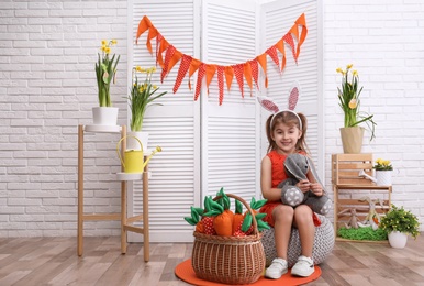 Adorable little girl with bunny ears, toy rabbit and carrots in Easter photo zone