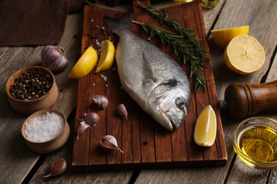 Photo of Raw dorado fish, lemon wedges, spices and oil on wooden table