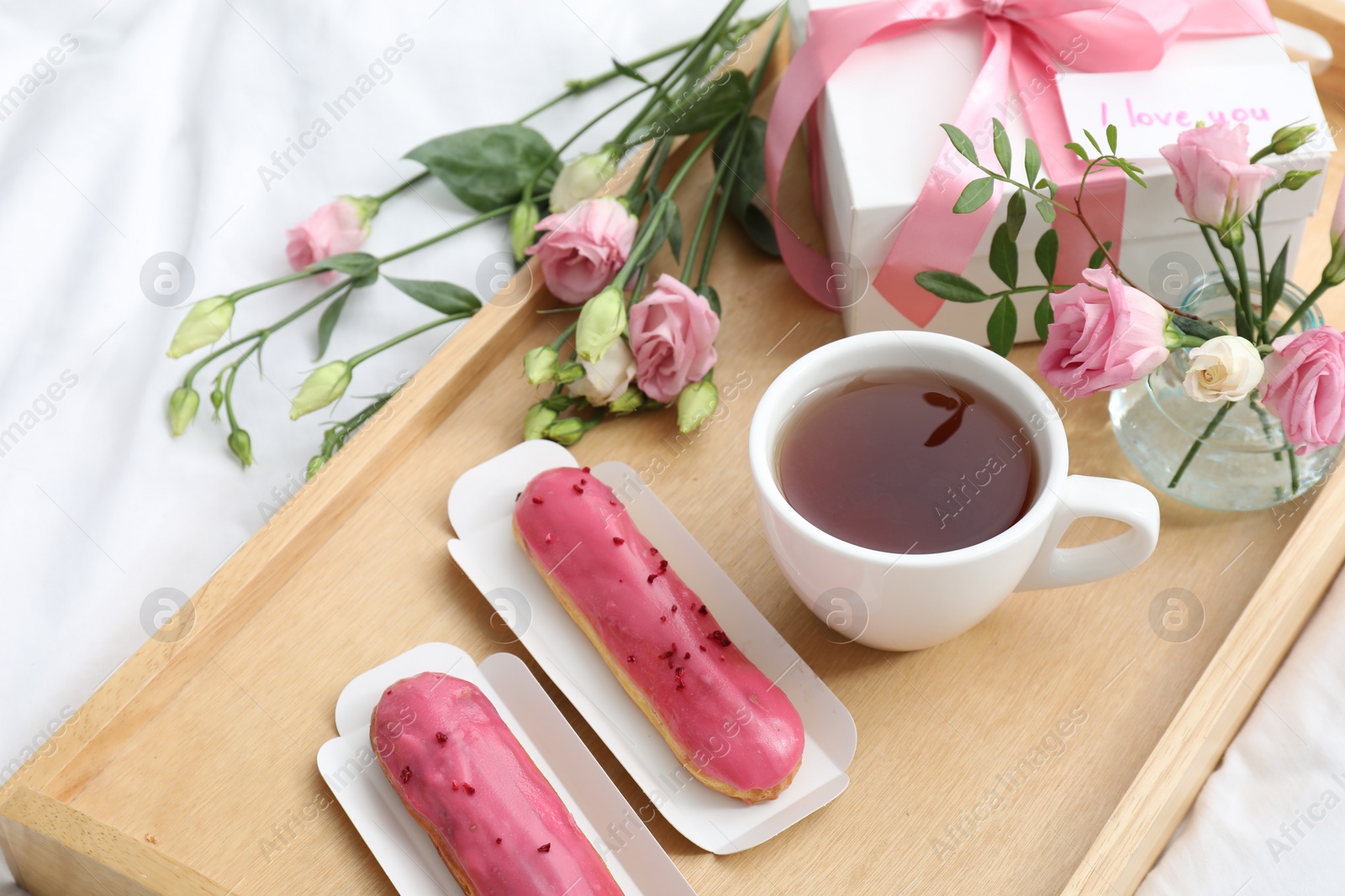 Photo of Tasty breakfast served in bed. Delicious eclairs, tea, gift box, flowers and card with phrase I Love You on tray