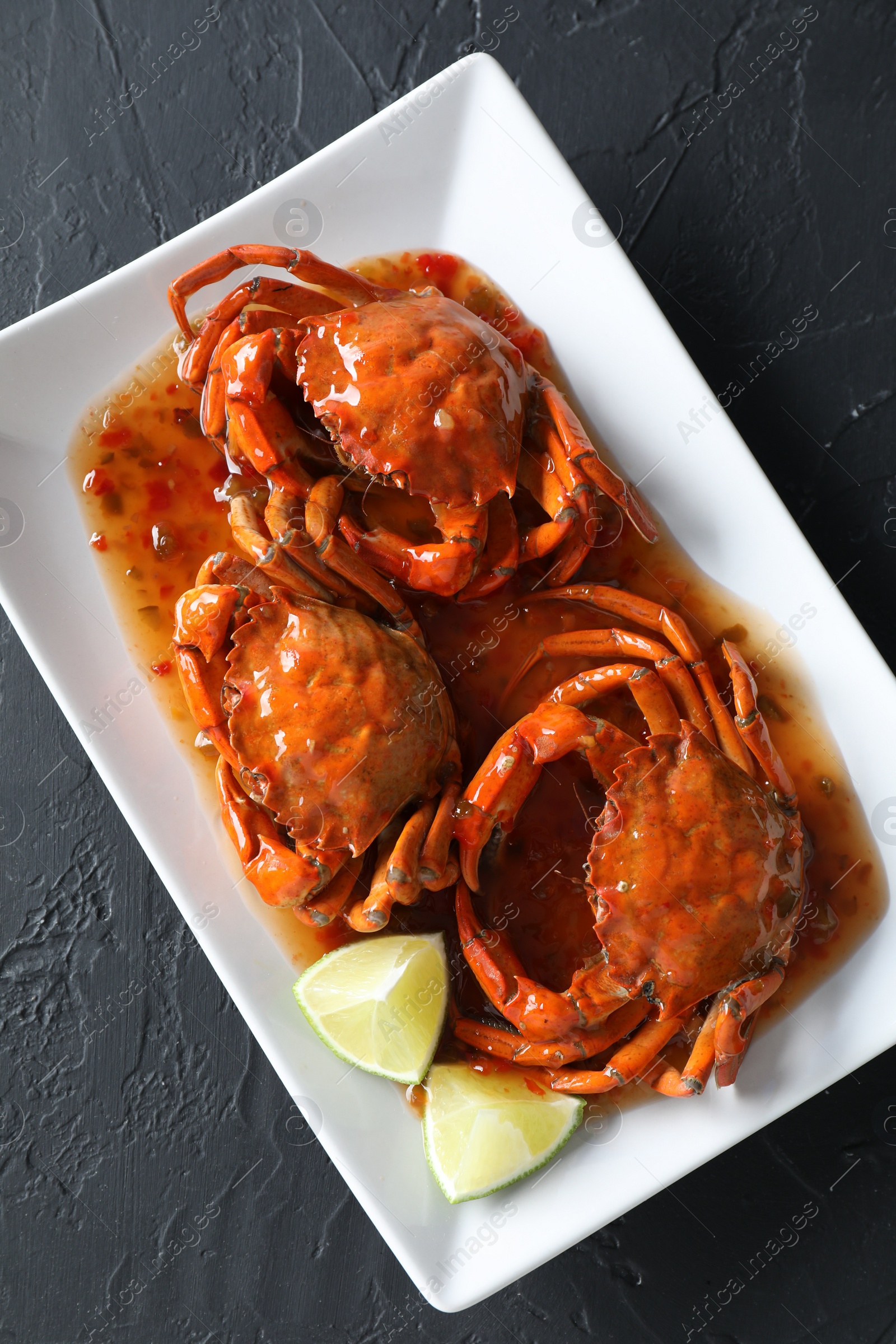 Photo of Delicious boiled crabs with sauce and lime on black textured table, top view