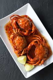 Delicious boiled crabs with sauce and lime on black textured table, top view