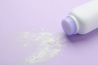 Bottle and scattered dusting powder on lilac background, closeup. Baby cosmetic product