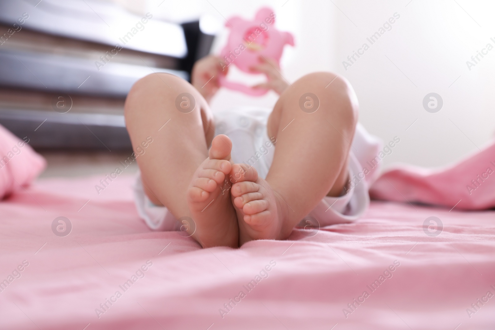 Photo of Little baby with toy on bed indoors, closeup