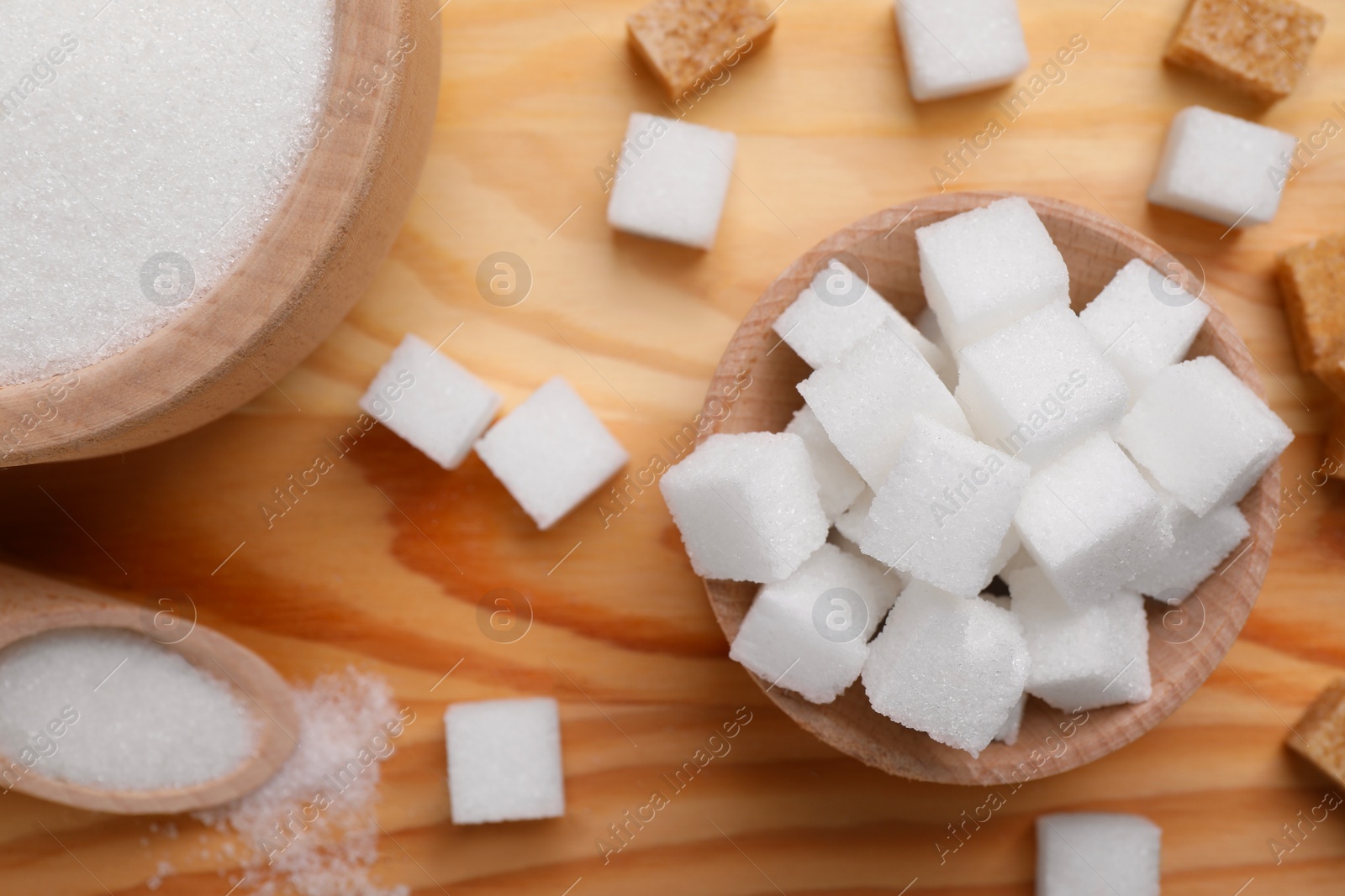 Photo of Bowls and scoop with different types of sugar on wooden table, flat lay