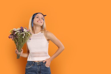 Happy hippie woman with bouquet of flowers on orange background. Space for text