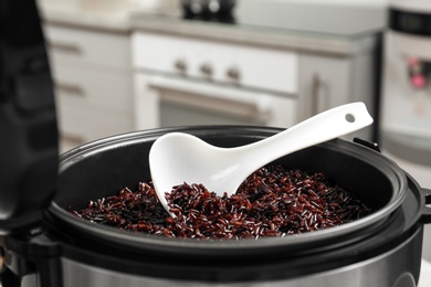 Photo of Modern multi cooker with spoon and boiled brown rice in kitchen, closeup
