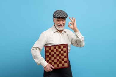Man with chessboard showing OK gesture on light blue background
