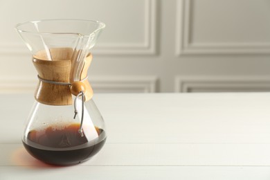 Glass chemex coffeemaker with coffee on white table, space for text