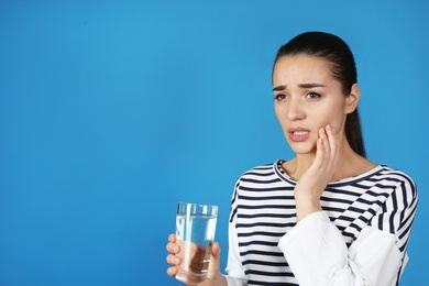 Photo of Emotional young woman with sensitive teeth and glass of water on color background. Space for text