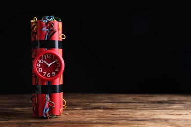 Photo of Dynamite time bomb on wooden table against black background. Space for text