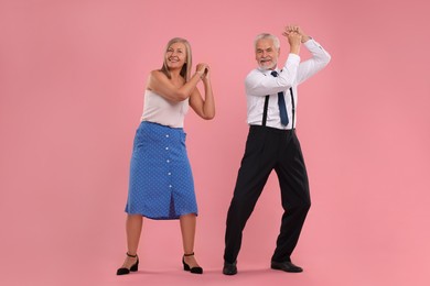 Senior couple dancing together on pink background