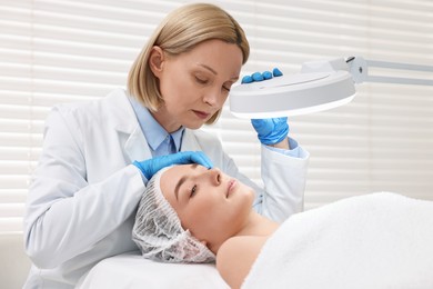 Photo of Dermatologist examining patient`s face under lamp in clinic