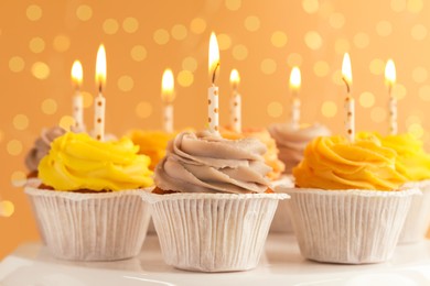 Photo of Tasty birthday cupcakes on white stand against blurred lights, closeup
