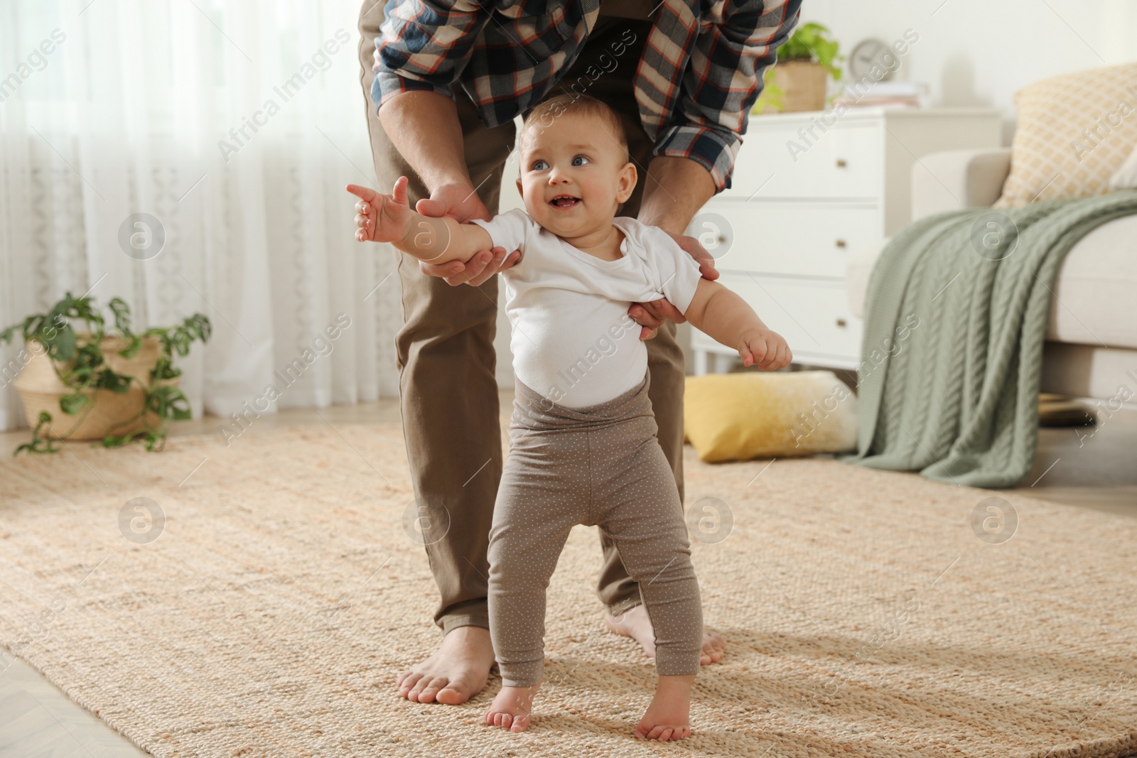 Photo of Father supporting his baby daughter while she learning to walk at home