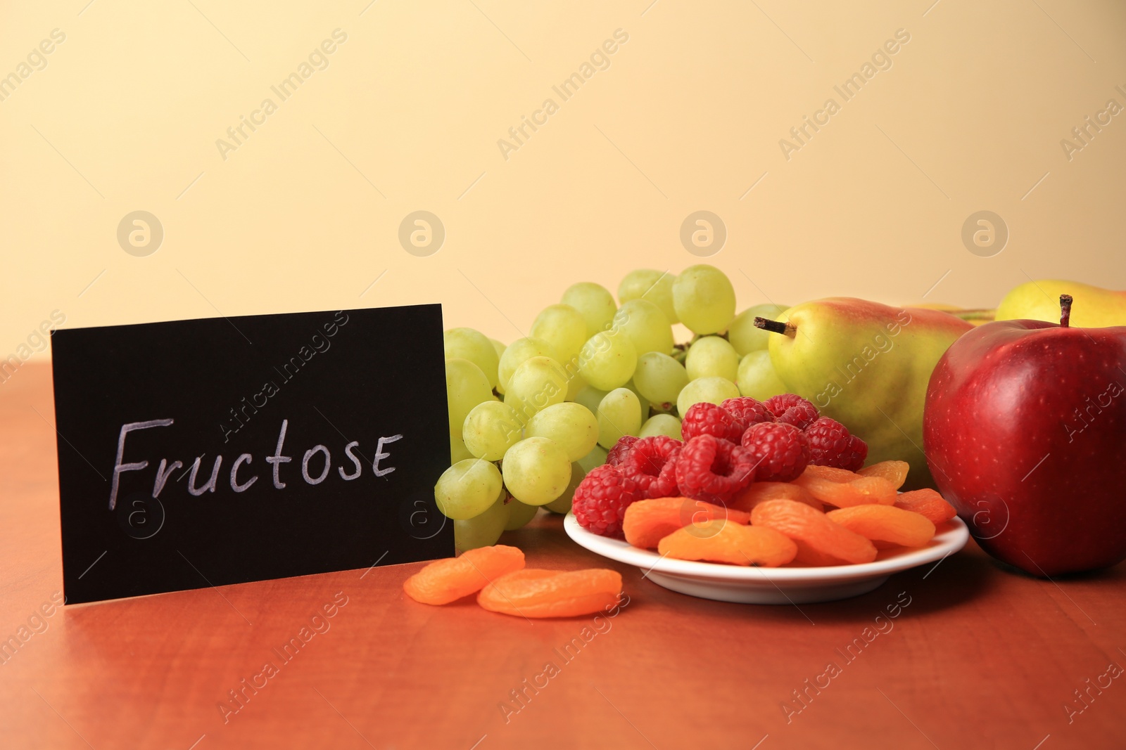 Photo of Card with word Fructose, delicious ripe fruits, raspberries and dried apricots on wooden table