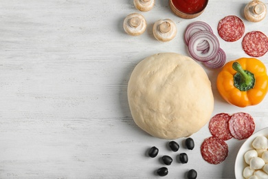 Flat lay composition with dough and ingredients for pizza on wooden table, space for text