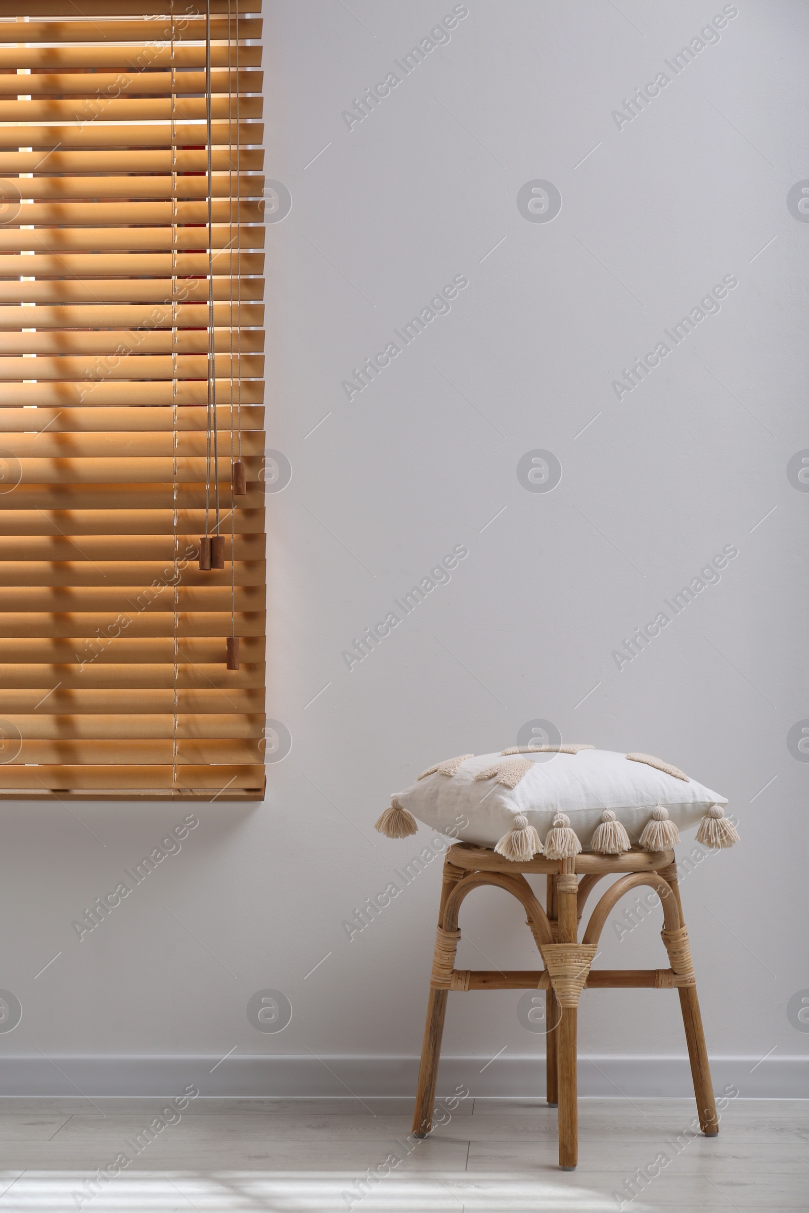 Photo of Wooden stool with cushion near light grey wall indoors. Interior accessory