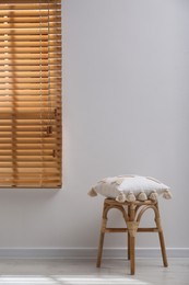 Photo of Wooden stool with cushion near light grey wall indoors. Interior accessory