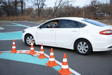 Photo of Young man in car on test track with traffic cones. Driving school
