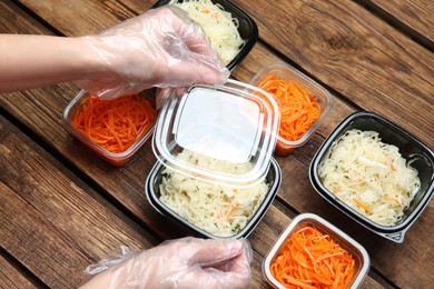 Waiter in gloves closing containers with salads at wooden table, closeup. Food delivery service