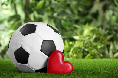 Photo of Football ball and red heart on green grass against blurred background. Space for text