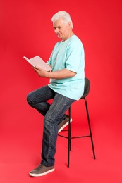 Senior man reading book on color background