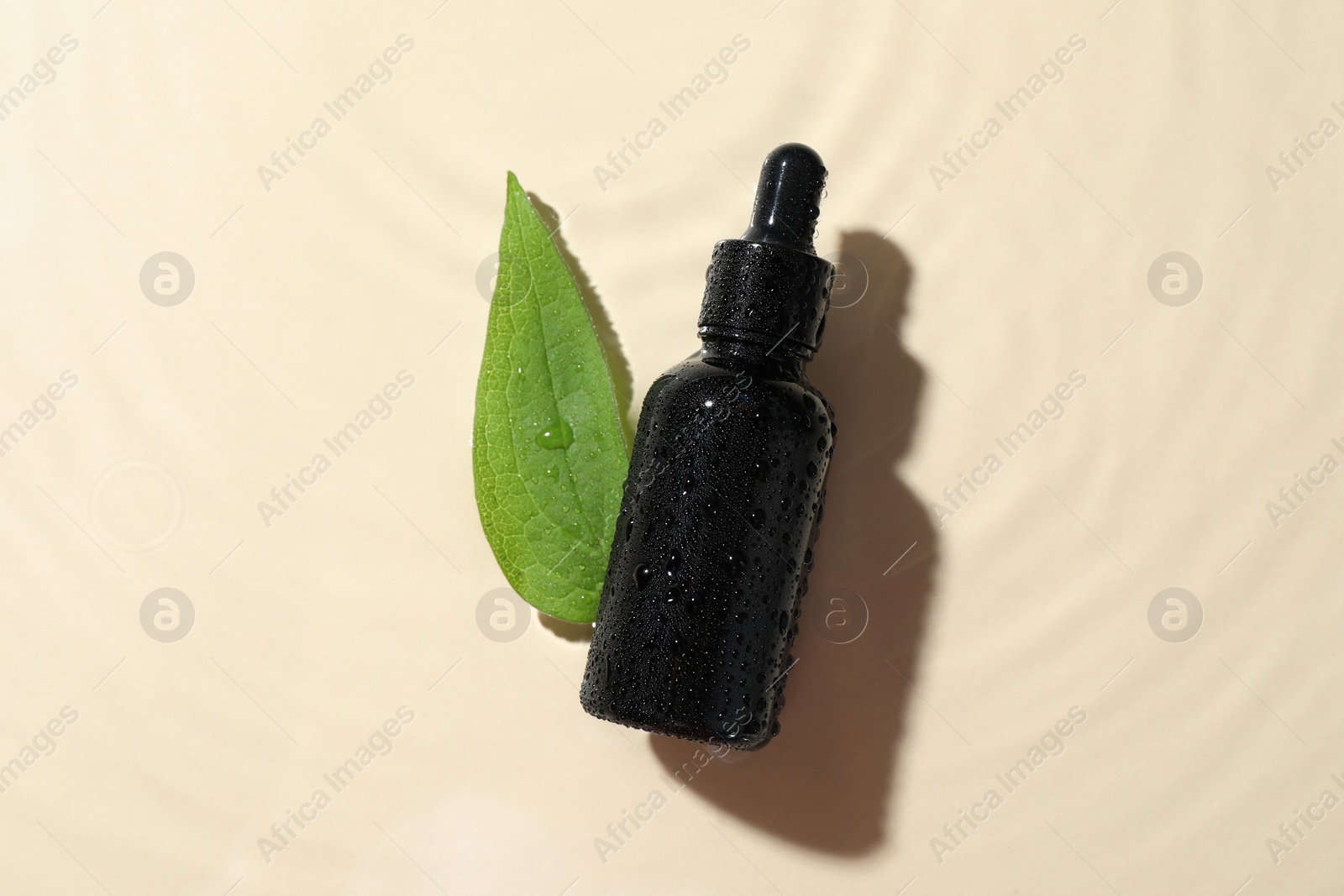 Photo of Bottle of cosmetic oil and green leaf in water on beige background, flat lay