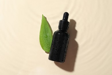 Bottle of cosmetic oil and green leaf in water on beige background, flat lay