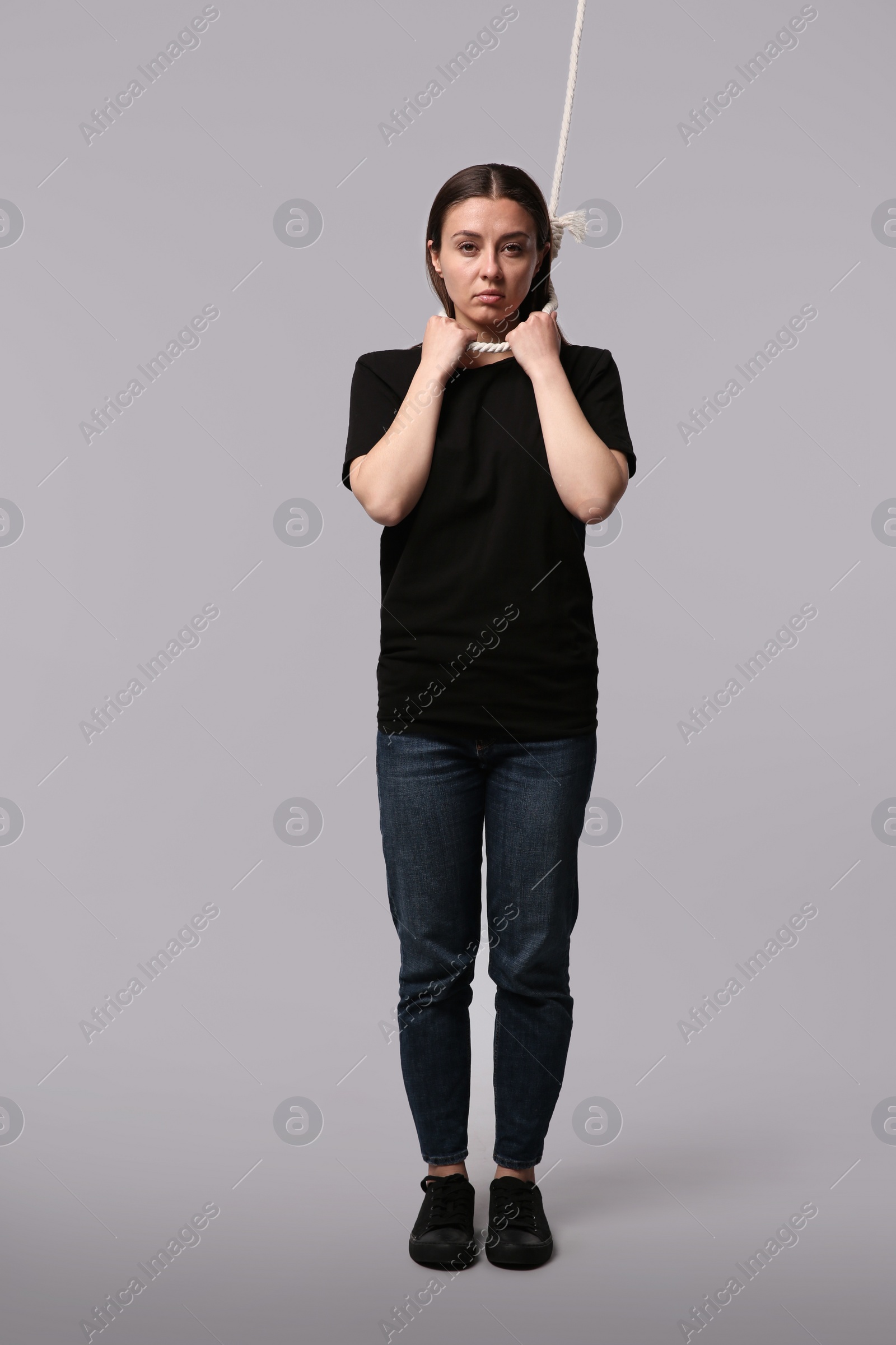 Photo of Depressed woman with rope noose on neck against light grey background