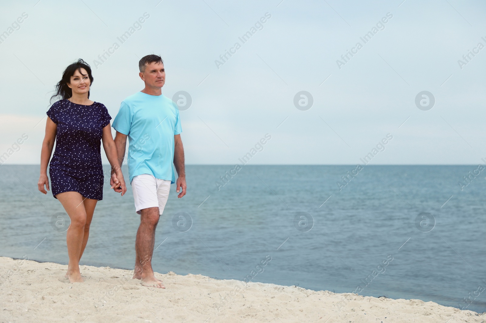Photo of Happy mature couple walking together on sea beach. Space for text