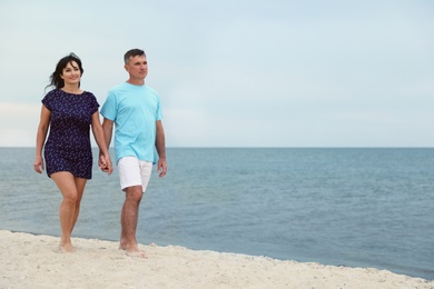 Happy mature couple walking together on sea beach. Space for text