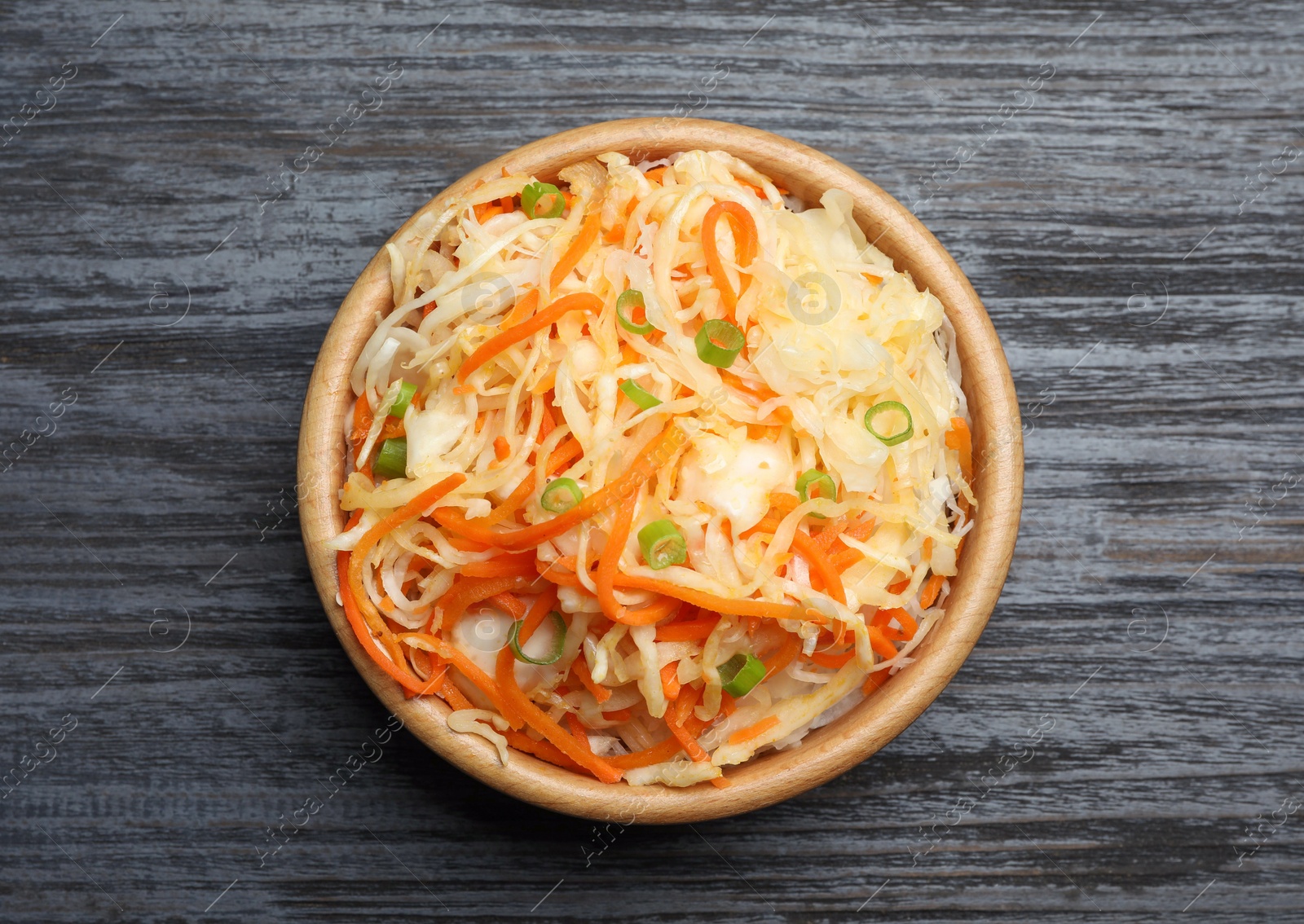Photo of Tasty fermented cabbage with carrot on black wooden table, top view