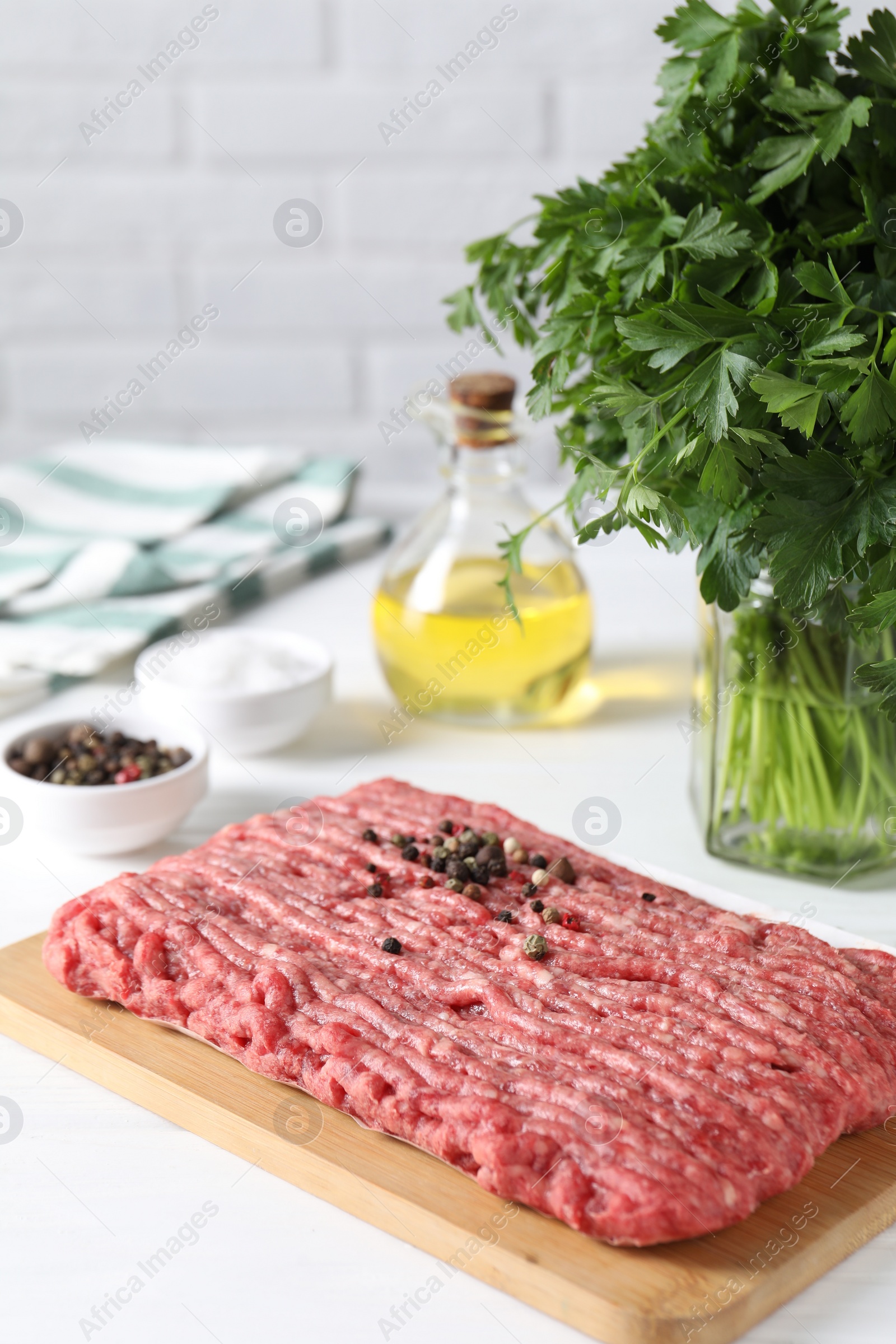 Photo of Raw ground meat, spices, oil and parsley on white table