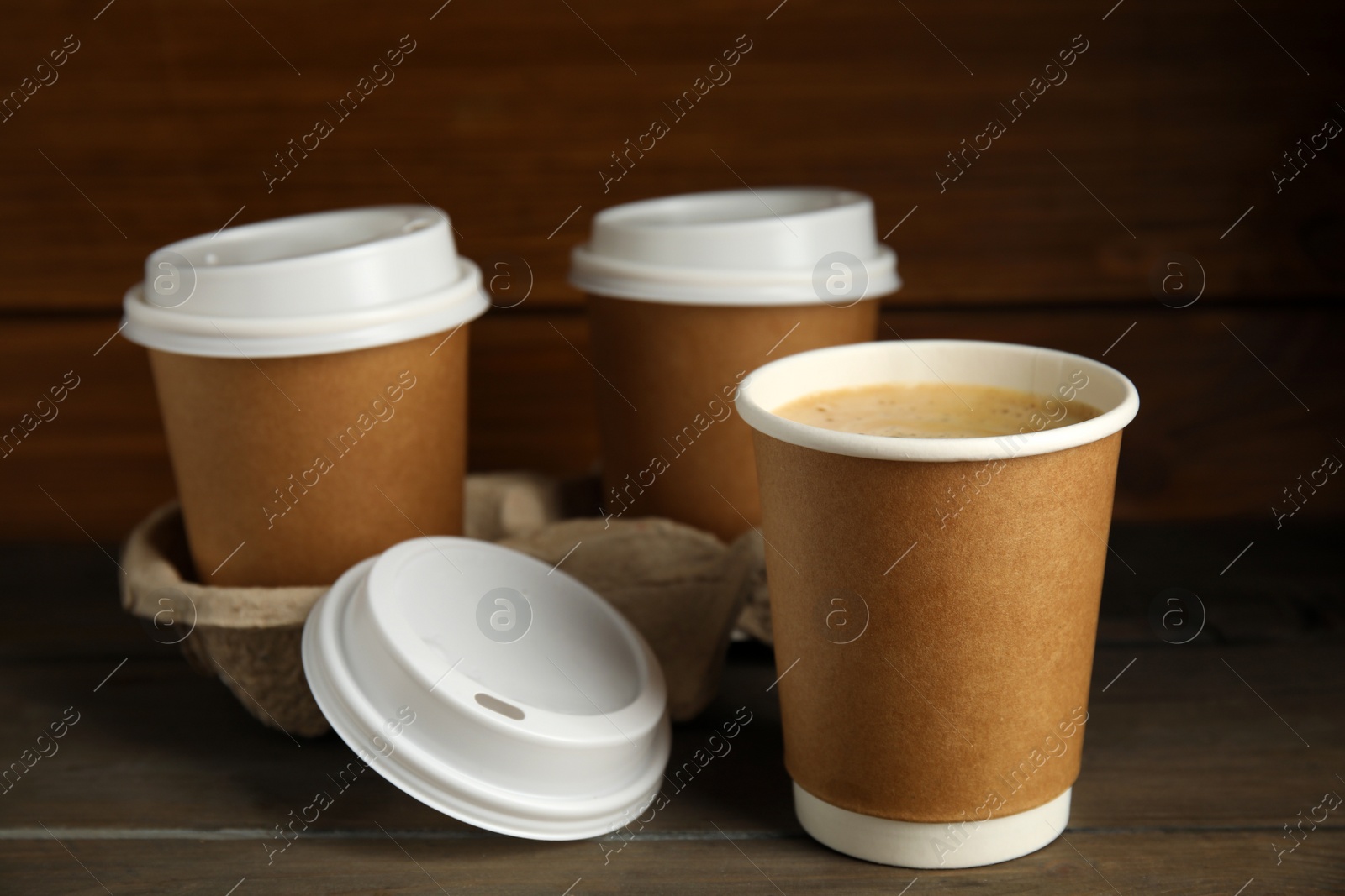 Photo of Takeaway paper coffee cups with plastic lids and cardboard holder on wooden table